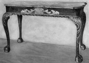 A Table of New York Make: The top is a shaped slab of gray marble with molded edge; the framework is carved and gilded. The ornamentation itself has elements of both the Queen Anne and early Georgian periods. These are central carved shell motif, carving of cabriole legs with boldly executed claw and ball feet. Together they date the piece about 1750. atableofnewyorkmake
