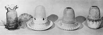 Illustration I: Four Elaborate Night Lamps in Colored Glass: Left to right: the first is of clear cranberry-red glass; second, blue mother-of-pearl base with crimped edge and shade of clear frosted glass; third, cranberry-red glass with decoration of white lines, circular and looped; and fourth, rose-and-white-flecked glass with ribbed shade. Illustration I: Four Elaborate Night Lamps in Colored Glass: Left to right: the first is of clear cranberry-red glass; second, blue mother-of-pearl base with crimped edge and shade of clear frosted glass; third, cranberry-red glass with decoration of white lines, circular and looped; and fourth, rose-and-white-flecked glass with ribbed shade.