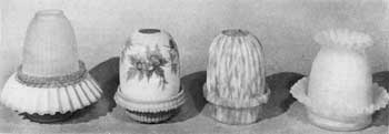 Illustration II: Four Other Designs of Night Lamps: That at the left has blue satin glass base with crimped edge and a frosted shade. Next, a lamp of Burmese glass with painted floral decoration. Then a lamp of simpler design in pink-and-white flecked glass and ribbed shade. At the right, a lamp of lemon-yellow satin-finish glass with crimping on both base and shade. Illustration II: Four Other Designs of Night Lamps: That at the left has blue satin glass base with crimped edge and a frosted shade. Next, a lamp of Burmese glass with painted floral decoration. Then a lamp of simpler design in pink-and-white flecked glass and ribbed shade. At the right, a lamp of lemon-yellow satin-finish glass with crimping on both base and shade.