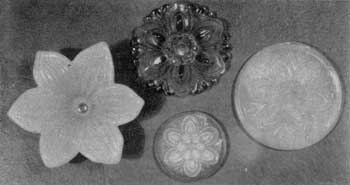 Four Sandwich Tieback Rosettes: Except for the one in the upper center, all are of opalescent glass. That at the lower left is a copy in glass of the clematis flower. The others are all of the same conventionalized floral design but show minor variations. Four Sandwich Tieback Rosettes: Except for the one in the upper center, all are of opalescent glass. That at the lower left is a copy in glass of the clematis flower. The others are all of the same conventionalized floral design but show minor variations.