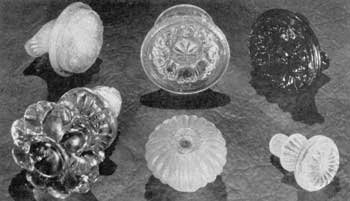 Fragments from Sandwich: Upper row, left to right: Conventionalized floral designs in opalescent, canary-yellow, and dark-blue glass. Lower row: Large rosette knob with glass screw shank (not found at Sandwich but attributed to it), broken, ribbed mushroom knob, and small knob with screcw-threaded shank. The last two are of clear glass that has become frosted from being buried in the ground. Fragments from Sandwich: Upper row, left to right: Conventionalized floral designs in opalescent, canary-yellow, and dark-blue glass. Lower row: Large rosette knob with glass screw shank (not found at Sandwich but attributed to it), broken, ribbed mushroom knob, and small knob with screcw-threaded shank. The last two are of clear glass that has become frosted from being buried in the ground.