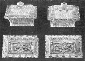 Illustration V - Covered Honey Dishes with Trays: These oblong covered dishes and trays, in Gothic pattern, are of like design except for the covers. One cover is curved, the other flat with two steps. Heart-bordered trays fit dishes although design differs. Trays are 7 inches long. Illustration V - Covered Honey Dishes with Trays: These oblong covered dishes and trays, in Gothic pattern, are of like design except for the covers. One cover is curved, the other flat with two steps. Heart-bordered trays fit dishes although design differs. Trays are 7 inches long.