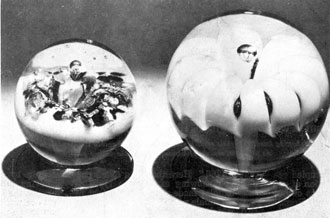 Two Millville Lily Paperweights: The footed example at the left, probably made by Marcus Kuntz, has a flower of turquoise blue with opal background. That at the right by John Rhulander is a lily formed of white glass with the stem very distinct, extending upward from the foot. Two Millville Lily Paperweights: The footed example at the left, probably made by Marcus Kuntz, has a flower of turquoise blue with opal background. That at the right by John Rhulander is a lily formed of white glass with the stem very distinct, extending upward from the foot.