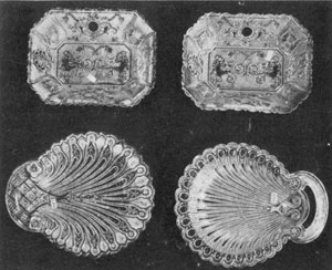 Illustration III - Pipes-of-Pan Trays and Two Shell Dishes: These pairs of trays are the only large Lacy Sandwich pieces with a design bearing anything like a human form. Dimensions 8 inches long. The two shell dishes, below, should be included among the choicest examples of Lacy glass. The dish at the left is in the Hairpin pattern. Dimensions, 9.5 by 8 inches. The dish at the right has the Peacock-Eye border. The open handle made this a difficult piece to produce. Dimensions, 9.5 by 7.75 inches. Illustration III - Pipes-of-Pan Trays and Two Shell Dishes: These pairs of trays are the only large Lacy Sandwich pieces with a design bearing anything like a human form. Dimensions 8 inches long. The two shell dishes, below, should be included among the choicest examples of Lacy glass. The dish at the left is in the Hairpin pattern. Dimensions, 9.5 by 8 inches. The dish at the right has the Peacock-Eye border. The open handle made this a difficult piece to produce. Dimensions, 9.5 by 7.75 inches.