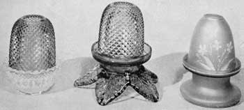 Illustration III: Three Other Designs: These are an example with clear base and amber shade in the "fine-cut" pattern; lamp with hand-wrought feet in leaf form, in dark green glass, light green "fine-cut" shade, and light red candle base; and lamp of frosted rose glass with applied floral decoration. Illustration III: Three Other Designs: These are an example with clear base and amber shade in the "fine-cut" pattern; lamp with hand-wrought feet in leaf form, in dark green glass, light green "fine-cut" shade, and light red candle base; and lamp of frosted rose glass with applied floral decoration.