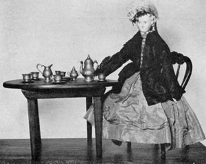 An American Doll of 1867: That was the year when she was won at a fair by a small boy. In disgust he banished her to the attic, so this doll with kid body and bisque head has survived in perfect condition. The original period dress of black and white silk is trimmed with royal blue, the same color as the coat. On the miniature table is a pewter tea set. An American Doll of 1867: That was the year when she was won at a fair by a small boy. In disgust he banished her to the attic, so this doll with kid body and bisque head has survived in perfect condition. The original period dress of black and white silk is trimmed with royal blue, the same color as the coat. On the miniature table is a pewter tea set.