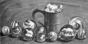 Glass Marbles of Various Designs: Those of swirled design predominated. Some are opaque or translucent, but with most of these clear glass was used for the casing. At the right of the tankard is a large marble with a sulphide figure of a boar in the center. Glass Marbles of Various Designs: Those of swirled design predominated. Some are opaque or translucent, but with most of these clear glass was used for the casing. At the right of the tankard is a large marble with a sulphide figure of a boar in the center.