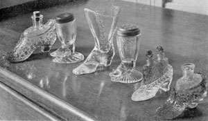 Illustration VIII: Other Shoe and Slipper Designs: The salt and pepper shakers in the center have perforated pewter tops. The slippers have the original perfume bottles for which they were made as holders. Illustration VIII: Other Shoe and Slipper Designs: The salt and pepper shakers in the center have perforated pewter tops. The slippers have the original perfume bottles for which they were made as holders.
