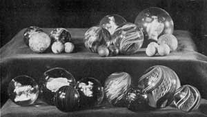 Typical Marbles That Collectors Seek: Upper row at the left, three large and two small ones of pottery; in the center, three glass shooters and small ones of clay; and right, a large glass one with sulphide center in shape of an eagle with four of clay with colored stripes. Lower row, left to right, three with sulphide centers, two of enamels and one of a fish. In front of them, one of slag glass. Next, one with opaque and irregularly swirled center. To the right and in center of this, a marble of amber glass with embedded metallic flecks. At the extreme right, two sizes of clear glass marbles with swirled center of colored threads. The technique employed in making these was approximately that used in paperweights of similar decorative design. Typical Marbles That Collectors Seek: Upper row at the left, three large and two small ones of pottery; in the center, three glass shooters and small ones of clay; and right, a large glass one with sulphide center in shape of an eagle with four of clay with colored stripes. Lower row, left to right, three with sulphide centers, two of enamels and one of a fish. In front of them, one of slag glass. Next, one with opaque and irregularly swirled center. To the right and in center of this, a marble of amber glass with embedded metallic flecks. At the extreme right, two sizes of clear glass marbles with swirled center of colored threads. The technique employed in making these was approximately that used in paperweights of similar decorative design.