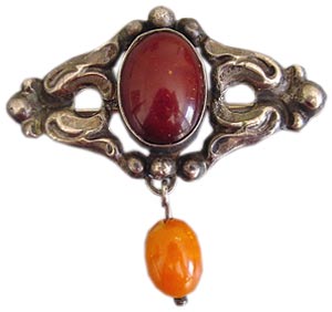 This Danish Arts & Crafts brooch from around 1910 features a burnt sienna cabochon in its center and an amber colored drop that swings freely below. This Danish Arts & Crafts brooch from around 1910 features a burnt sienna cabochon in its center and an amber colored drop that swings freely below.