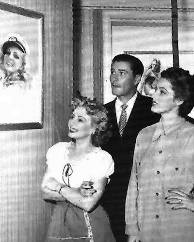 zoe6 Mozert shows her work to Errol Flynn and Eleanor Parker, the stars of 1946's "Never Say Goodbye." The artist served as a consultant and provided the art for the film, which features Flynn as a George Petty-type pin-up painter. Via "Tease!"#3.