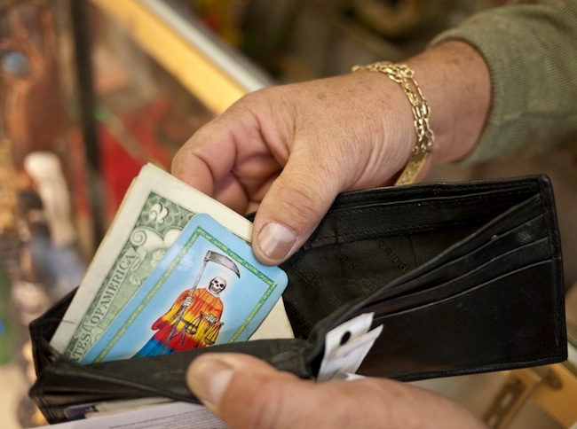 morbid_santa5 A Santa Muerte worshiper reveals a card in his wallet at Botánica de la Santa Muerte in Los Angeles. (Photo by Joanna Ebenstein, via Morbid Anatomy)