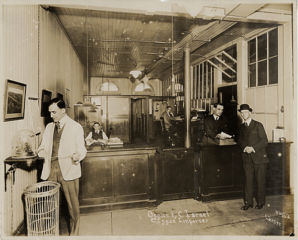 In 1917, coffee importer A.C. Israel of New Orleans had a ticker that spat out the latest coffee prices. The ticker's overflow was captured in a tall wicker waste paper basket. Photo via <a href="http://www.officemuseum.com/photo_gallery_1910s%20ii.htm">Early Office Museum</a>.