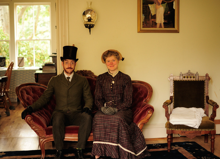 The Chrismans sit in their parlor on a couch from the 1890s. A gas lantern is installed on the wall above them. (Photo courtesy Estar Hyo-Gyung Choi, Mary Studio, via ThisVictorianLife.com)