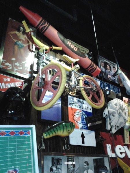 At a Friday's in the 2010s, a BMX bicycle hangs among pop culture memorabilia referencing "Ghostbusters," "Star Wars," Wonder Woman, and the 1965 World's Fair. (Via BMX Museum Forum)