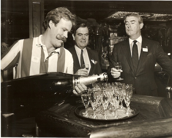 Dan Scoggin, right, watches a bartender pour champagne from a giant bottle. (Via Friday's Founder)