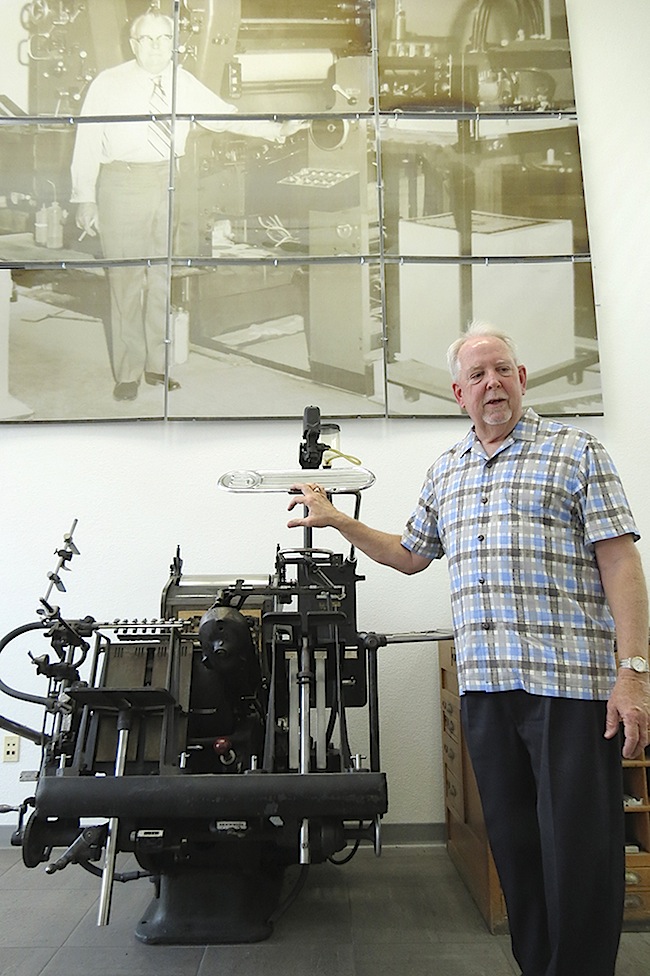 Jack Stoughton, Jr. stands next to his company's first Heidelberg "Windmill" letterpress. Behind him is a photomontage made out of aluminum printing plates of his father, Jack Stoughton, Sr.