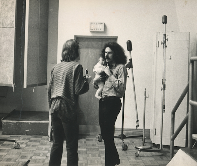 In a photo by Bob Cato, photographer Bob Seidemann is seen holding a band member's baby while talking with Big Brother's road manager, David Richards.